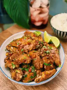 A plate of Thai Inspired Spicy Chili Lime Chicken Wings served with lime wedges and a bowl of rice