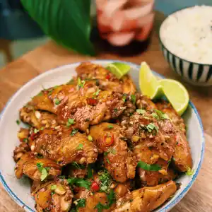 A plate of Thai Inspired Spicy Chili Lime Chicken Wings served with lime wedges and a bowl of rice