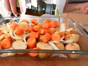 Adding olive oil into a pan of root vegetables like potatoes, carrots, and onions before adding a whole roast chicken on top
