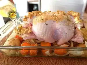 Adding white wine into the pan of vegetables and whole chicken on top for Roast Chicken