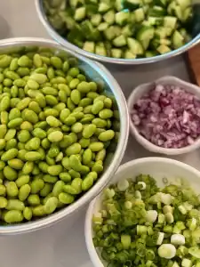 Ingredients for sesame edamame salad, including edamame, cucumber, green onion, and red onions