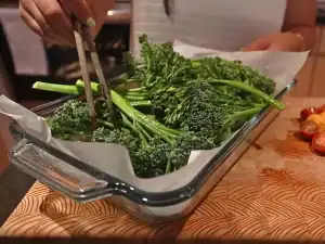 Mixing fresh brocollini seasoned with olive oil, salt, and pepper before roasting in the oven for Lemon Parmesan broccoini