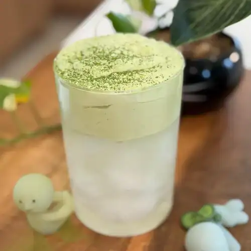 A glass of Matcha Coconut Cloud made with matcha cold foam and coconut water garnished with extra matcha powder