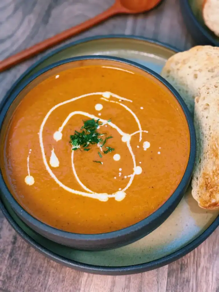 A close up of a bowl of Roasted Vegetable Soup with a little coconut milk topping. Served with toasted bread.