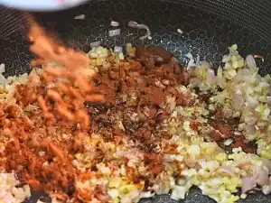 Adding spice mix to shallots, garlic, and ginger for Singaporean Chicken Curry