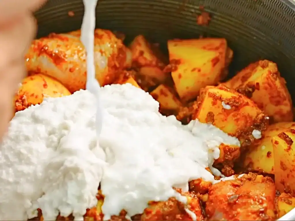 Adding coconut cream to spiced chicken and potatoes for Singaporean Chicken Curry