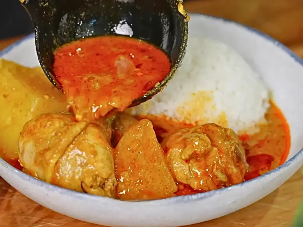 Scooping Singaporean Coconut Curry into a bowl with steamed rice
