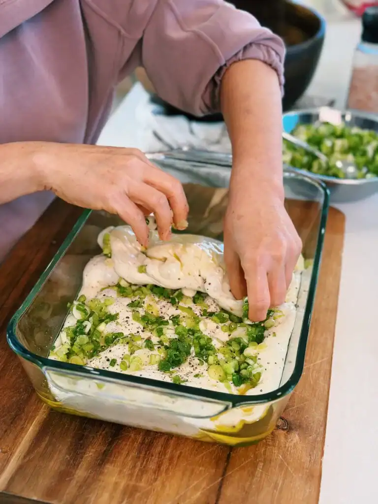 Rolling the focaccia dough over the scallion oil mix inside the baking pan. 