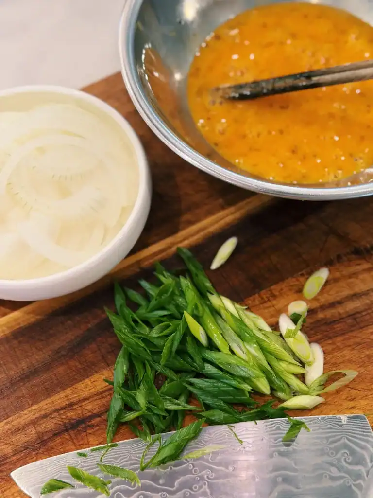 Ingredients for Japanese Chicken and Egg Rice Bowl, including chopped onions, beaten egg, and shopped green onions