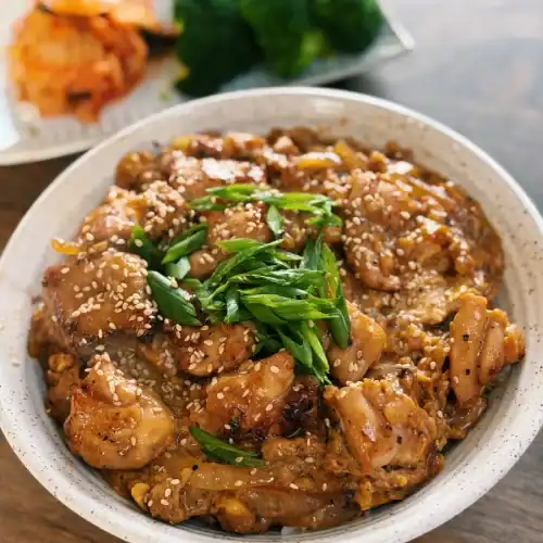 Japanese Inspired Chicken Egg Rice Bowl served with green onion and sesame seeds as well as side dishes in the background