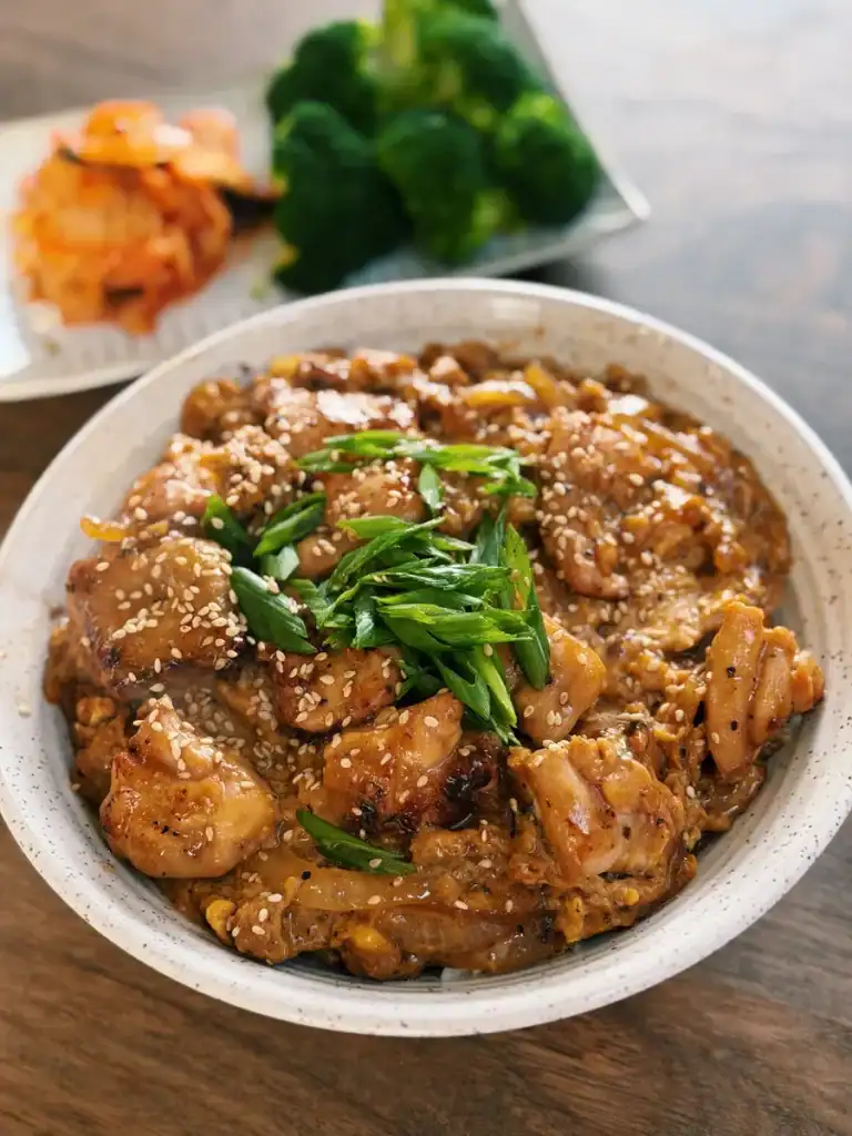 Japanese Inspired Chicken Egg Rice Bowl served with green onion and sesame seeds as well as side dishes in the background