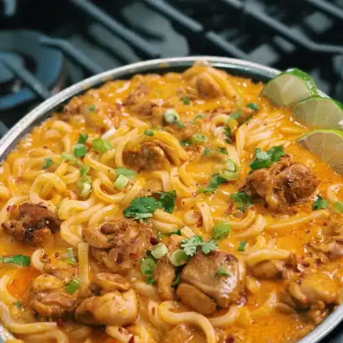 Coconut Curry Chicken Udon in a nonstick pan served with lemon slices and cilantro