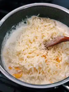Adding shredded cheese to cheesy sauce to add to Creamy Cheesy Cauliflower Bake
