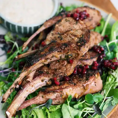 Rosemary Garlic Lamb Chops served on micro baby greens with creamy dill sauce and garnished with pomegranate seeds