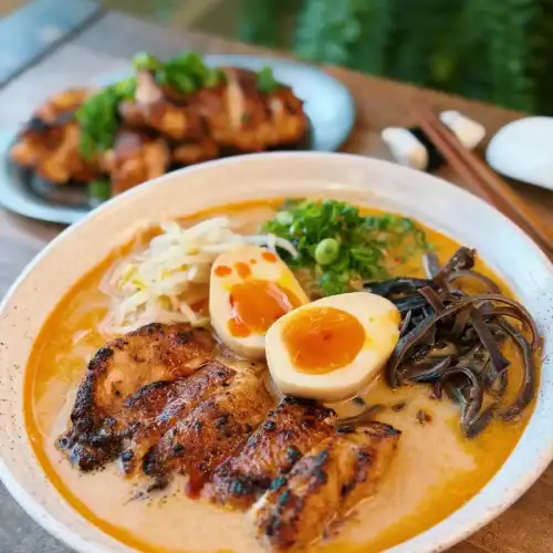 A bowl of miso chicken ramen with sliced pan-fried chicken, a halved ramen egg, and various toppings