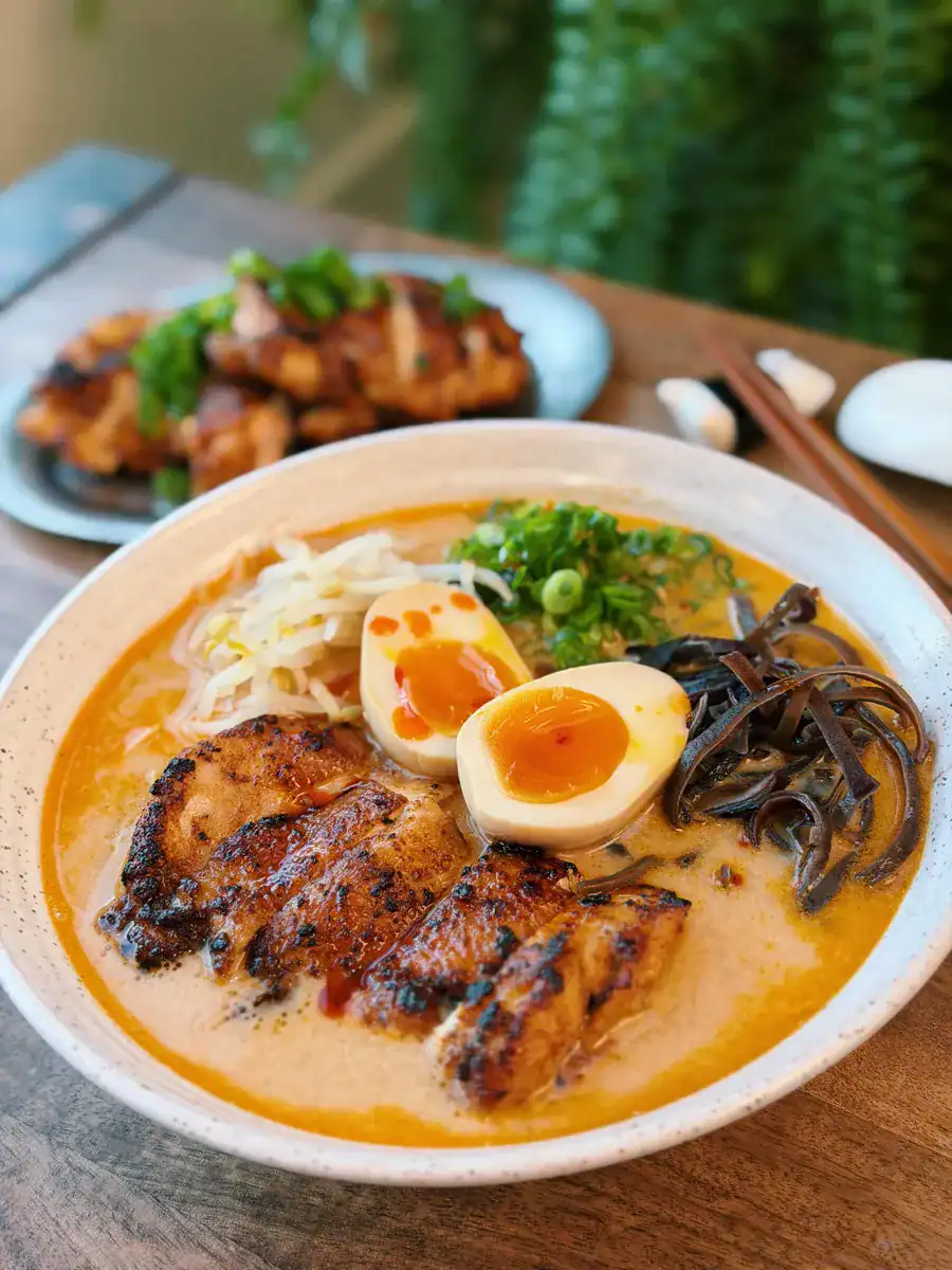 A bowl of miso chicken ramen with sliced pan-fried chicken, a halved ramen egg, and various toppings
