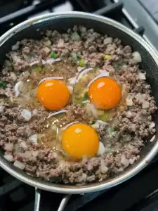Adding 3 eggs into a pan full of ground beef for minced beef and egg rice