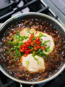 3 Eggs simmering in a sauce of ground beef in a pan for Minced Beef and Egg rice