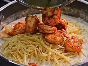 Adding cooked shrimp and pasta back into the pan of Alfredo sauce for Shrimp Alfredo Pasta