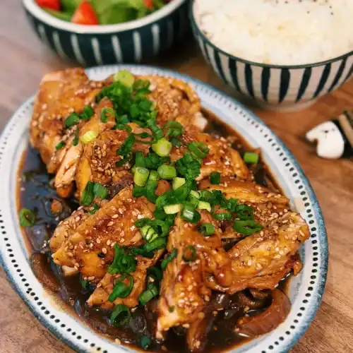 A plate of Soy Glazed Apple Chicken served with rice and salad