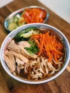 A bowl of Braised chicken Noodle Soup with shredded braised chicken, sauteed carrots, and garlic zucchini