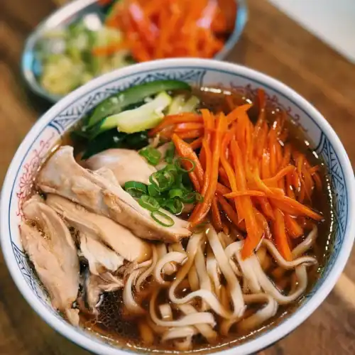 A bowl of Braised chicken Noodle Soup with shredded braised chicken, sauteed carrots, and garlic zucchini