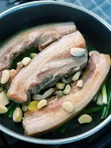 Lining the bottom of the pan with aromatics like garlic, ginger, and green onion for orange glazed pork