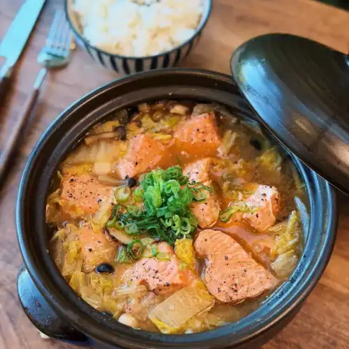 A pot of Miso Salmon Stew served with green onion on top and a bowl of rice on the side