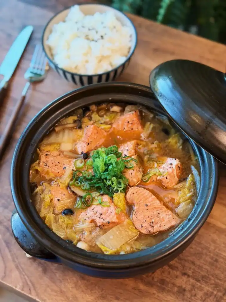 A pot of Miso Salmon Stew served with green onion on top and a bowl of rice on the side