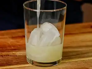 Adding pineapple juice into a glass of ice for Pineapple Soju Cocktail