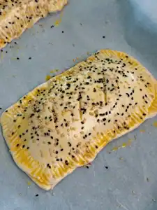 Assembled Crab Rangoon hand pie with sesame seeds and egg wash