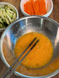 Beating eggs for egg ribbons to make Vegetable Noodle Soup