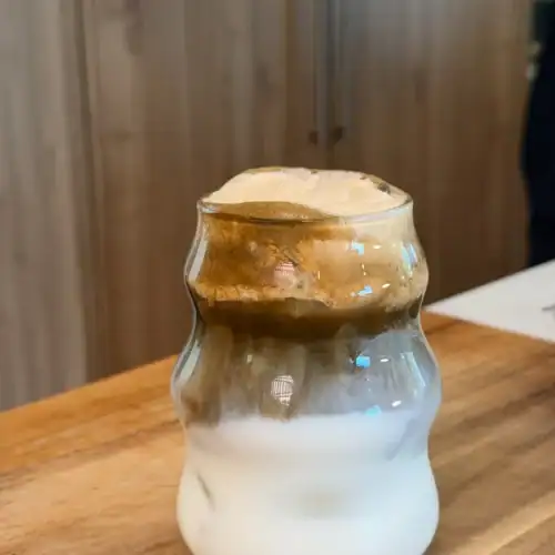 A glass of Pumpkin Spice Hojicha Latte, with layers of milk, hojicha, and pumpkin spice cold foam