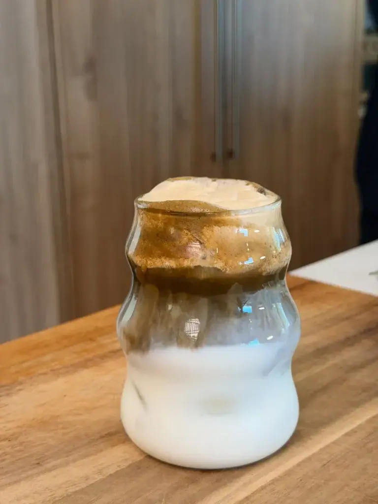 A glass of Pumpkin Spice Hojicha Latte, with layers of milk, hojicha, and pumpkin spice cold foam