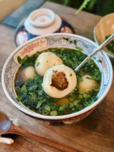A bowl of savory Tang Yuan in light broth with a bite taken out of one showing the pork mushroom filling inside
